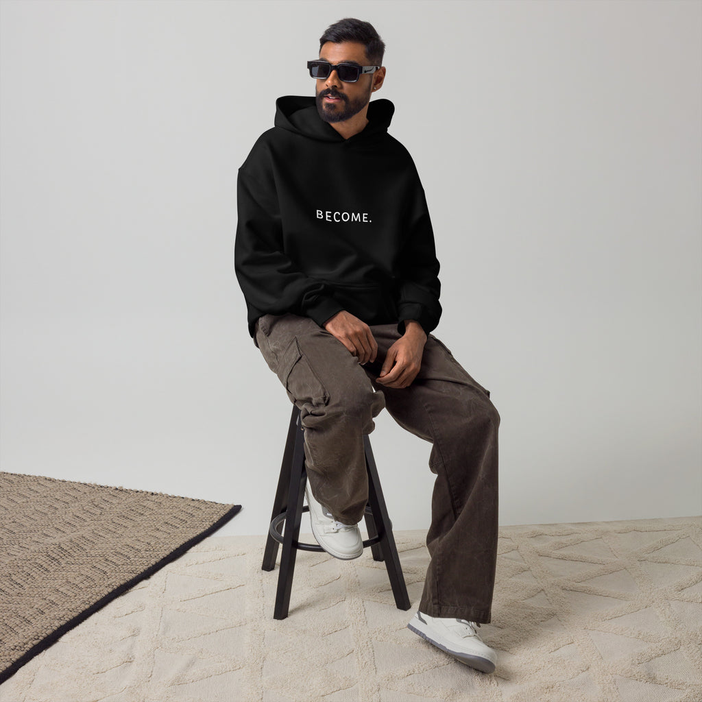 Man wearing the BECOME. Oversized Hoodie in Black, front view with BECOME. printed across the chest