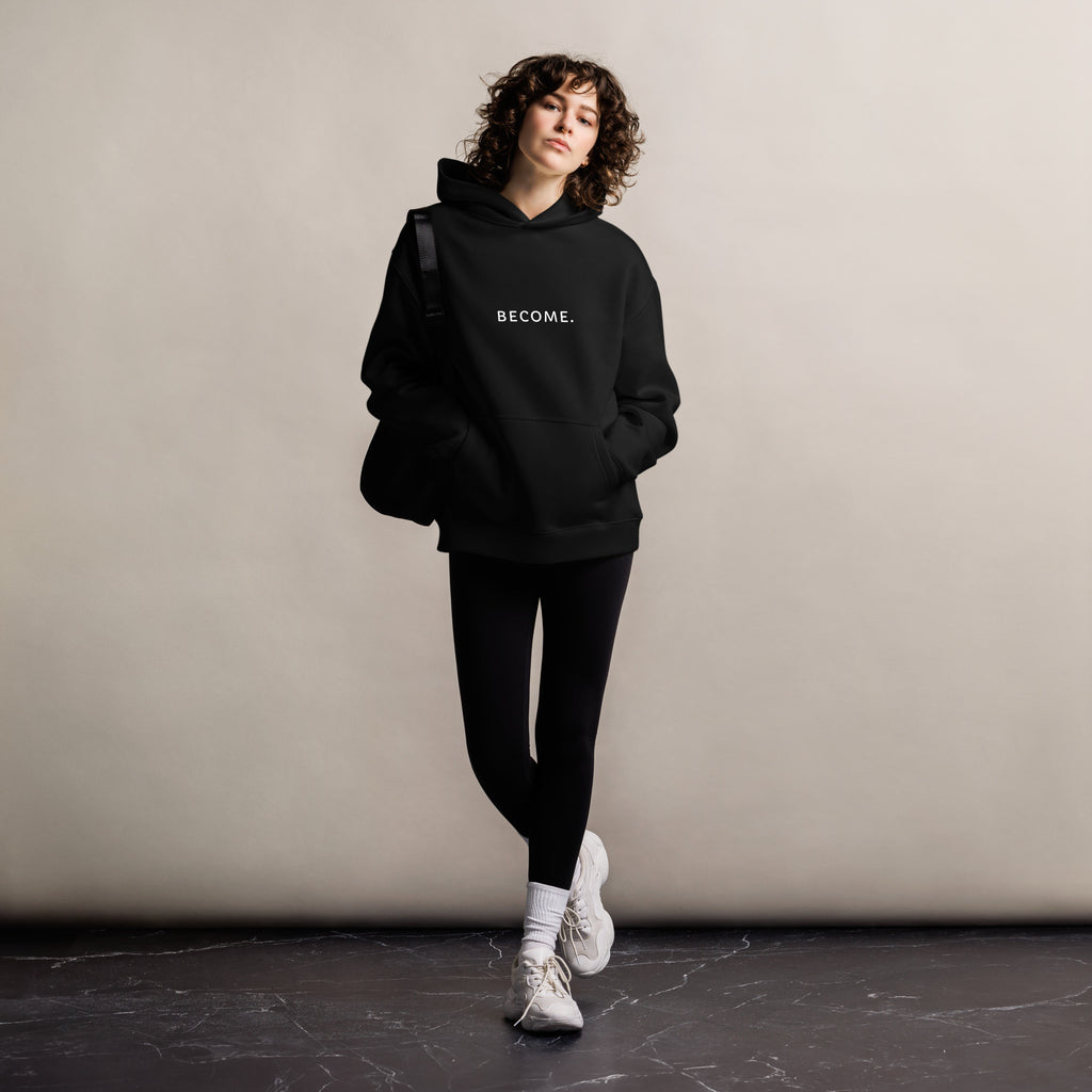 Woman wearing the BECOME. Oversized Hoodie in Black, front view with BECOME. printed across the chest