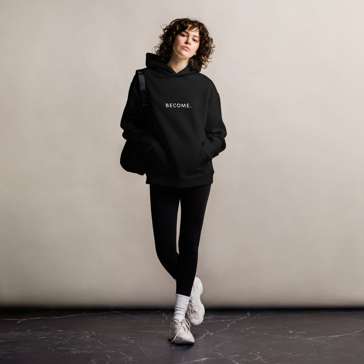 Woman wearing the BECOME. Oversized Hoodie in Black, front view with BECOME. printed across the chest